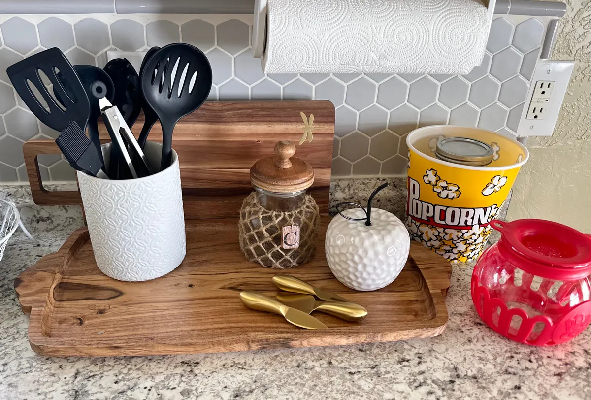 A homey, detail-rich scene focused on a set of kitchen utensils, a decorative popcorn container, and a cutting board, suggesting preparations for entertaining or enjoying snacks during a movie night. The surrounding decor feels cozy and lived-in.