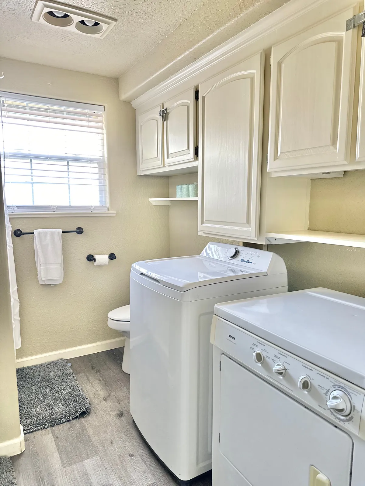 A serene laundry nook with both a washing machine and dryer, ample cabinetry for storage, and a window letting in natural light. The space feels calm, practical, and tucked away, perfect for efficient laundry routines without visual clutter.