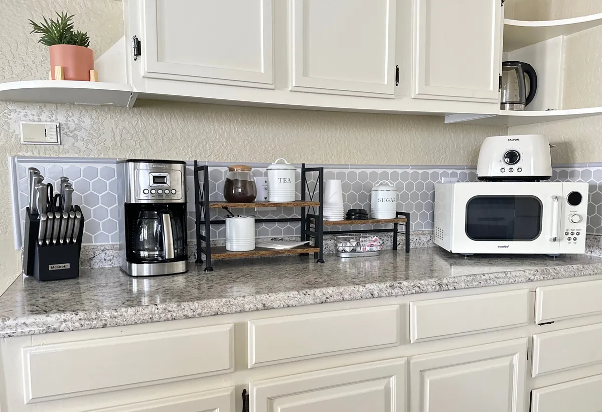 A cozy kitchen corner with a coffee maker, stacked shelves, microwave, cutlery holder, and tea canister, inviting guests to brew a fresh cup or prepare quick meals. The scene is intimate and highlights small yet important kitchen details.
