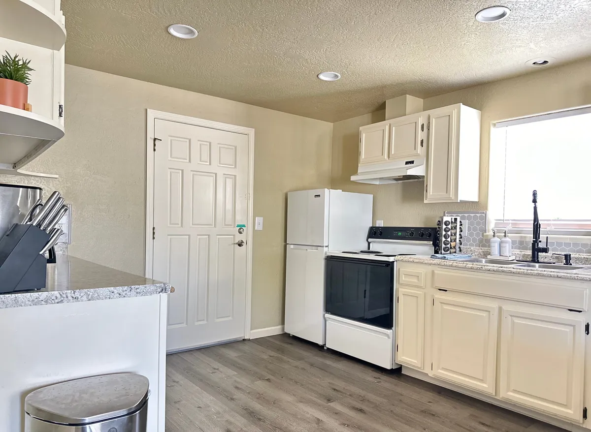 A welcoming, well-lit kitchen featuring modern appliances, a spacious countertop, and a window letting in plenty of natural light. The setup suggests it's fully equipped for preparing meals, with ample space for family or group cooking.
