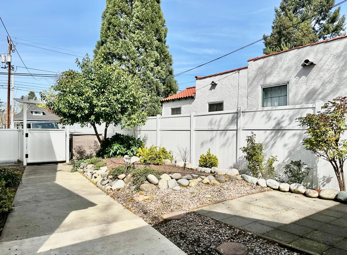 A peaceful exterior view showcasing a pathway winding through a neatly maintained garden area, featuring trees, a fence, and inviting green space. The setting exudes tranquility and privacy.