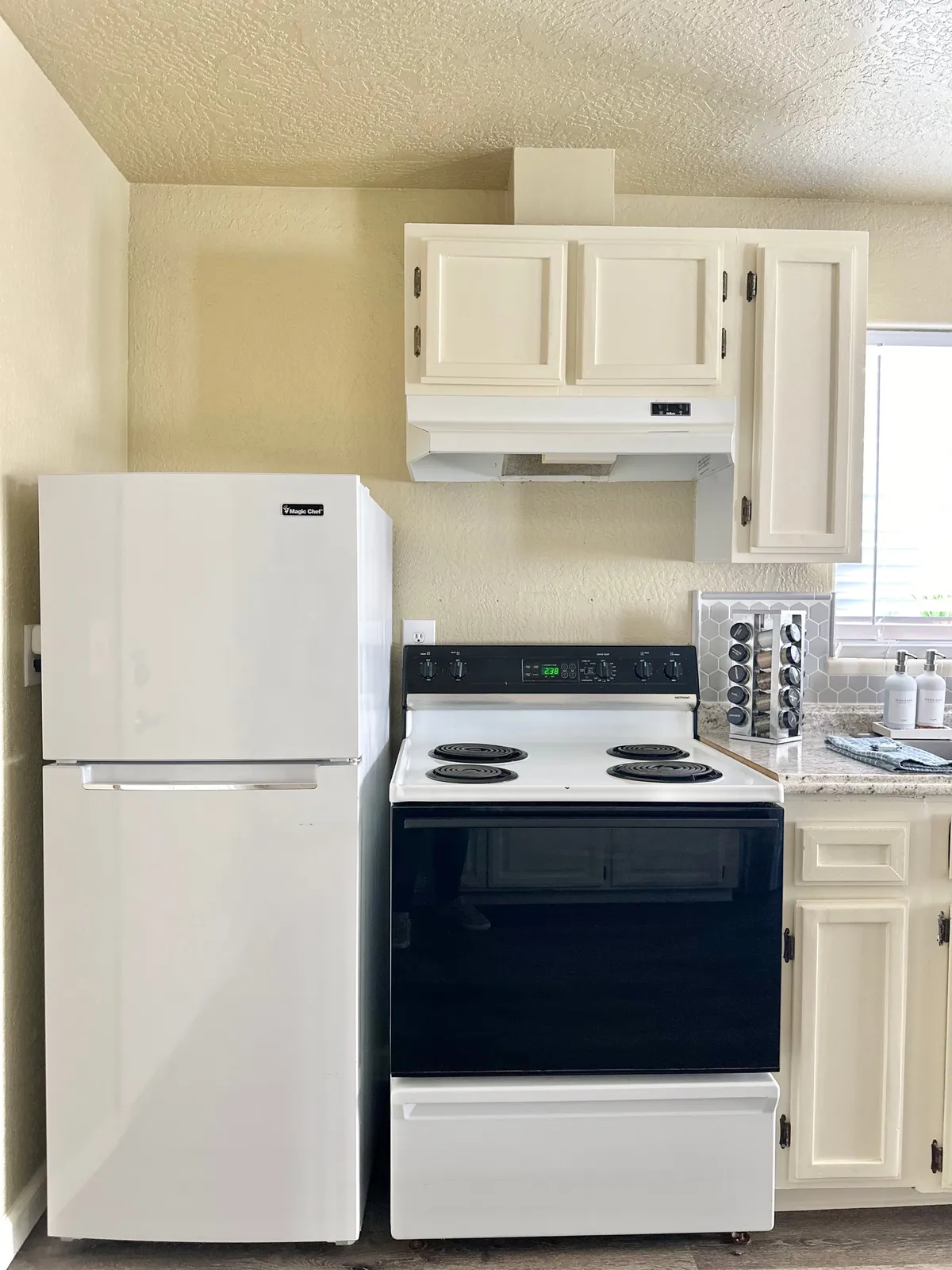 A well-lit kitchen featuring a stove, full-size refrigerator, ample cabinetry, and a spacious countertop, providing a clear view of the core cooking area. The overall scene is welcoming and emphasizes both functionality and comfort.