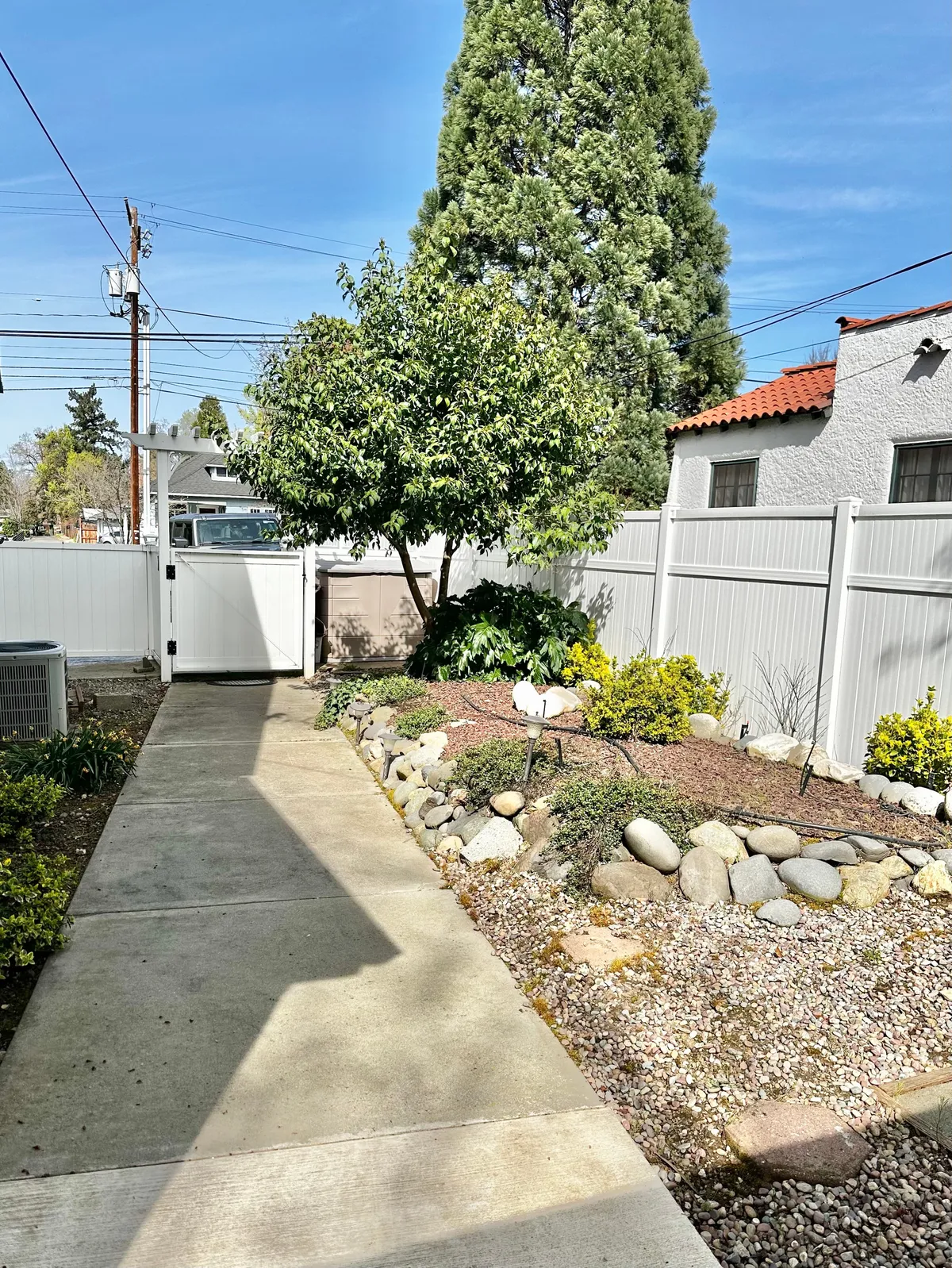 An inviting outdoor space with a green tree, a clear pathway, vibrant flower beds, and a sturdy fence. The area appears safe, quiet, and perfect for a refreshing walk or a moment of relaxation.