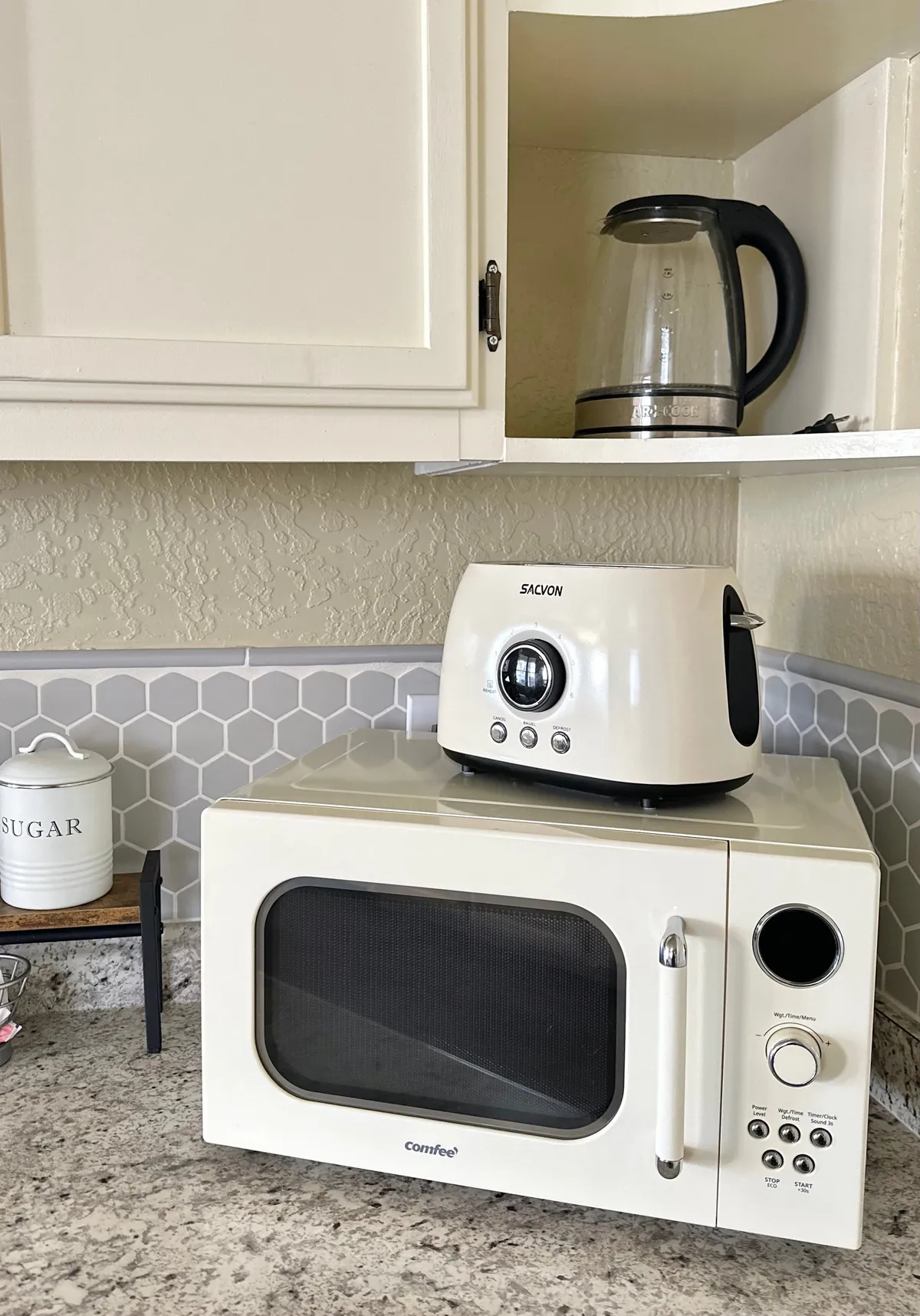 A welcoming kitchen setup featuring a microwave, toaster, kettle, and sugar container on the countertop. The space is homey and functional, ideal for preparing quick meals or enjoying a relaxing cup of tea after a busy day.