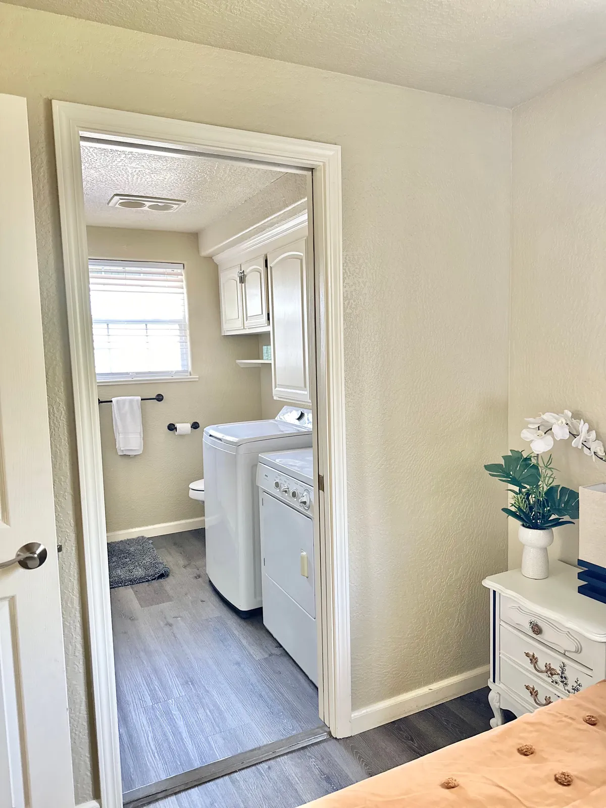 A thoughtfully designed laundry area featuring a modern washer and dryer, set within bright white cabinetry. A decorative plant and a textured rug add warmth and homeliness, while the organized shelving and storage create a tidy, uncluttered space.